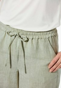 Helle grüne Leinenhose mit elastischem Bund, verstellbarem Kordelzug und Seitentaschen. Glatte Textur, lockere Passform.