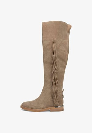 Bottes en daim beige montantes à la cheville avec une semelle plate, présentant des franges longues le long du côté extérieur et un accent en forme de boucle à l'arrière.