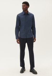 Camisa azul marino con un diseño estampado, de mangas largas, con cuello abotonado, combinada con pantalones oscuros y mocasines negros.