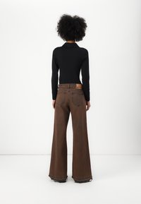 Brown wide-leg pants with a raw hem and contrasting stitching, paired with a black long-sleeve top, viewed from the back.
