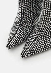 Botas de tacón alto negras con diseño de punta afilada, adornadas con numerosos brillantes plateados que aportan una apariencia texturizada.