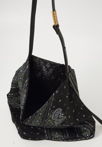 Melnas auduma plecu soma ar baltu un zaļu paisley rakstu, regulējamu siksnu ar zeltītām burtiem, kas veido vārdu "PINKO," atvērta augšdaļa, kas parāda iekšējo kabatu.