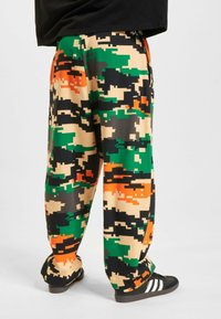 Multifarvet camouflagebukser i grøn, sort og orange, lavet af blødt stof, med en afslappet pasform og elastisk talje.