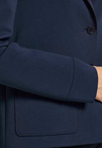 Marineblauer Blazer mit glatter Textiloberfläche, einer Einzelknopfverschluss und einer Vordertasche mit sauberen Nähdetails.