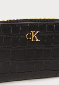 Black wallet with crocodile texture, gold "cK" logo, and gold zipper along the top edge.
