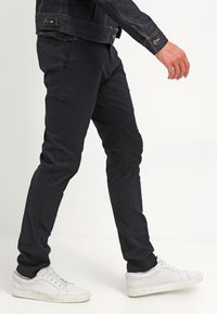 Schwarze Slim-Fit-Hosen aus Baumwollmischung mit glatter Textur, dezenten Nähten, kombiniert mit weißen Turnschuhen.