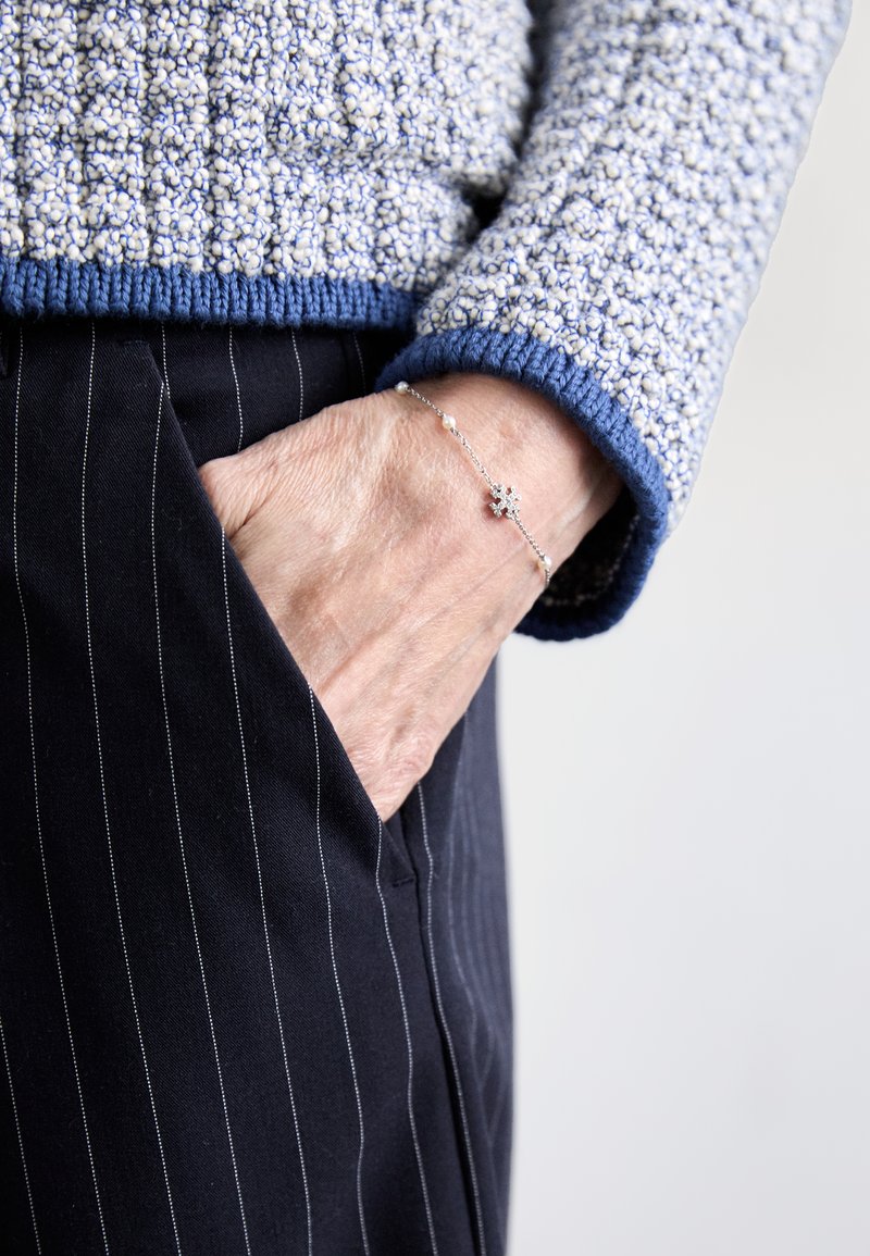 Lietots zils un krēms teksturēts džemperis ar zilu apakšu, apvienots ar melnām svītrām biksēm. Sudraba aproce ar ziedu dizainu uz rokas.