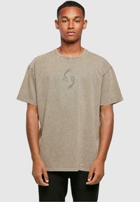 Kortærmet, oversized, beige bomulds T-shirt med rund halsudskæring og grå fiskegrafik på brystet. Diskret vasket struktur.