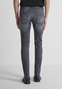 Jeans ajustados en gris con una textura desgastada, con bolsillos traseros y costuras en contraste, combinados con calzado negro.