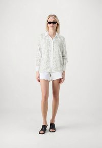 Φαρδιά γκρι ανοιχτόχρωμο μοτίβο σακάκι με λευκό γιακά, σε συνδυασμό με λευκά σορτς με ξεφτισμένα τελειώματα και μαύρα ανοιχτά mule παπούτσια.