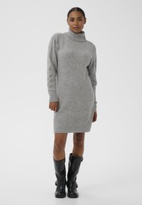 Robe en tricot gris à col roulé avec des manches longues, des poignets et un ourlet côtelés. Portée avec des bottes noires jusqu'au genou. Texture lisse, silhouette ajustée.