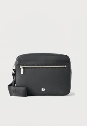 Zwarte rechthoekige crossbodytas met voorvak met ritssluiting, zilverkleurige hardware en verstelbare stoffen riem met gestructureerd patroon.