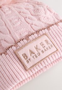 Lyserød strikket hue med tekstureret kabelmønster, ribstrikket kant og en blød rektangulær label med "BAKER by TED BAKER" i gyldent tråd.