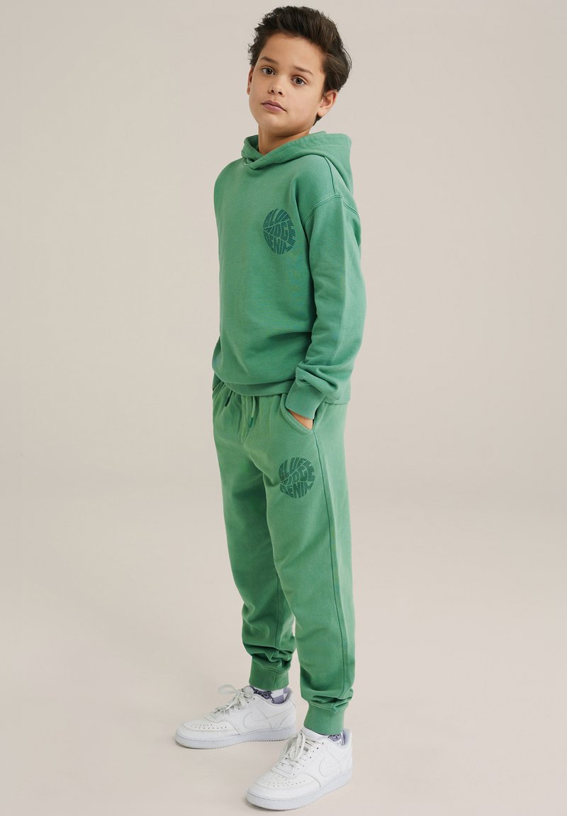 Conjunto de sudadera y pantalones verdes hechos de tela suave. La sudadera cuenta con un bolsillo frontal y un estampado de logo; los pantalones tienen tobillos con puños y bolsillos laterales.