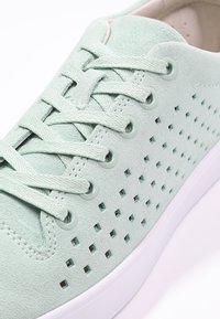 Světlé zelené semišové tenisky s perforovaným designem, odpovídajícími tkaničkami a šedým kováním, s bílou gumovou podrážkou. Texturovaný vrchní povrch.