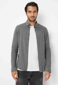Graues Hemd mit langen Ärmeln, leichtem Stoff und Kragen. Über einem weißen T-Shirt getragen, kombiniert mit dunklen Jeans.