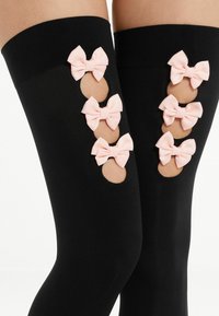 Bas noirs jusqu'à la cuisse avec des découpes, présentant trois nœuds en satin rose, créant un design ludique. Texture douce et lisse.