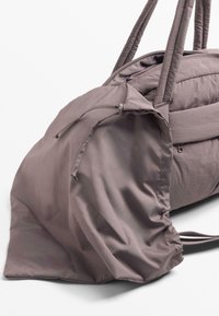 Sac de sport mauve avec des extrémités arrondies, fermeture à cordon et poignées rembourrées, sur fond blanc.