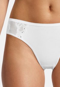 Weiße Baumwollunterwäsche mit einem Spitzenbesatz an den Seiten, verziert mit floralen Mustern und einer glatten, nahtlosen Textur.