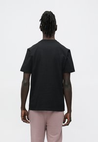 Juodas medvilninis marškinėlis laisvo silueto, trumpomis rankovėmis ir apvalia kaklo iškirpte. Lygios tekstūros, paprasto dizaino, be matomų logotipų ar raštų.