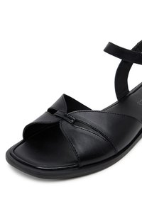Sandalia de cuero negro con punta cuadrada, diseño de tiras cruzadas y correa en el tobillo. Textura suave con suela plana de goma.