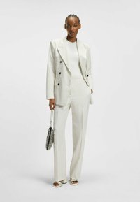 Gestreept lichtcrème pak met een dubbelzijdige blazer, bijpassende op maat gemaakte broek en open-teen sandalen. Een zilveren kettinghandtas accentueert de look.