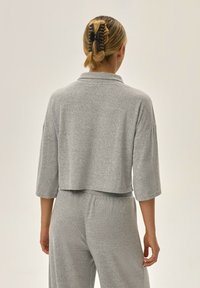 Szary krótki sweter z długimi rękawami, wykonany z miękkiego materiału. Ma złożony kołnierz i luźny krój, dopasowany do podobnych szarych spodni.