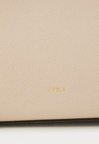 Beige leren portemonnee met een gestructureerd oppervlak, voorzien van een gouden "FURLA" logo. De randen zijn omlijnd in het zwart, wat een contrast biedt met de hoofd kleur.