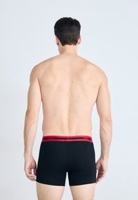 Schwarze Baumwoll-Boxershorts mit einem roten Logo-Bund, die eine körpernahe Passform und eine glatte Textur bieten. Von hinten betrachtet.