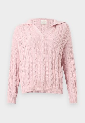 Pull en maille torsadée rose clair à manches longues et col en V sur un fond gris clair uni.
