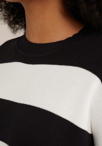 Maglione a righe bianche e nere con collo a girocollo a costine e una morbida consistenza in maglia. Primo piano del tessuto e del collo, che mette in evidenza le righe a contrasto.