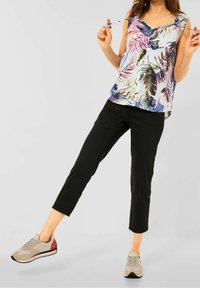 Top sin mangas de flores con escote en V, con patrones de hojas multicolores. Pantalones recortados negros y zapatillas beige con acentos rojos.