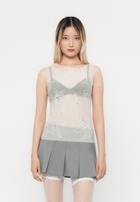 Top in grigio trasparente con ricami floreali e decorazioni, abbinato a una minigonna plissettata grigia e pantaloni corti con pizzo sotto.