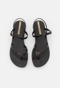Black plastic sandals with a textured sole, featuring two crisscrossing straps and a buckle, accented by a gold strip on the footbed.