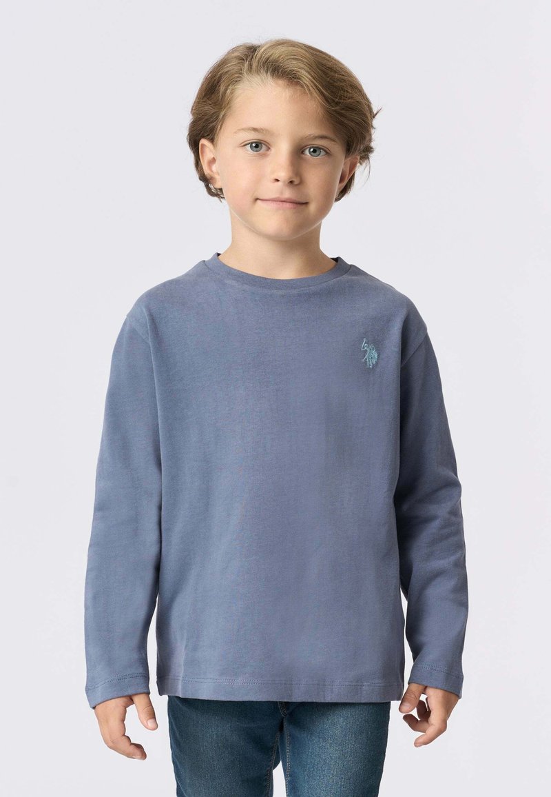 Camicia a maniche lunghe in cotone azzurro chiaro con colletto tondo e un piccolo logo ricamato sul petto, abbinata a jeans blu.