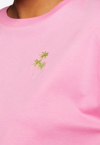 Närbild av en rosa skjorta med små gröna broderade palmträd på bröstområdet.