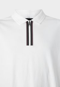 Fehér póló, rövid cipzárral, fekete és piros csíkkal a galléron. Elegáns, sima, pamutszerű anyagból készült.