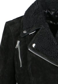 Černá semišová motorkářská bunda s huňatým černým límcem, stříbrnými kovovými prvky a asymetrickým zipovým zapínáním. Celkově hladká textura.