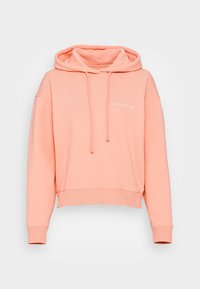 Kaptur z miękkiego materiału w kolorze brzoskwiniowym, charakteryzujący się krótkim krojem, szerokimi rękawami oraz małym białym napisem z przodu.