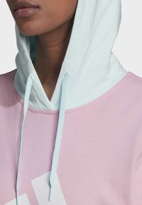 Felpa rosa chiaro con cappuccio verde menta e lacci. Presenta una texture liscia e un grande logo bianco sulla parte anteriore.