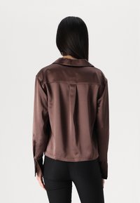 Brown satin shirt with long sleeves and a collared neckline, featuring a back pleat and side slits, viewed from the back.