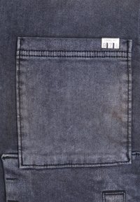 Mörkblå denimaterial med en stor, sydd ficka på baksidan. Har en silveretikett med "DIESEL IND" och en numerisk kod.