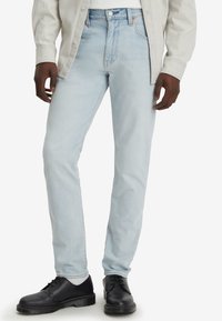 Hellblaue Denim-Jeans mit geradem Schnitt, Fünf-Taschen-Design und leicht verblasster Textur, kombiniert mit schwarzen Schnürschuhen.