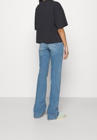 Svart kortärmad t-shirt i lös passform, tillsammans med ljusblå utsvängda jeans. Jeansen har en klassisk femfickdesign och en subtil blekning.