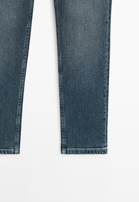 Donkerblauwe spijkerbroekspijpen vanaf halverwege de dij zichtbaar met rechte zoom op een witte achtergrond.