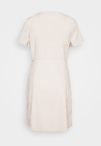 Robe beige à manches courtes dans une coupe décontractée. Sa texture lisse présente un design simple avec un col rond et une taille cintrée.