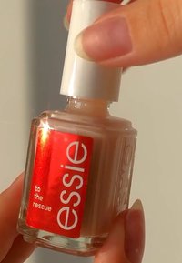 Bottiglia di smalto per unghie con una base in vetro rettangolare trasparente, liquido beige chiaro, tappo bianco e etichetta rossa con la scritta "essie" e "to the rescue."