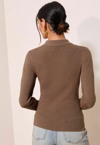 Brauner, gerippter Strickpullover mit langen Ärmeln und Kragen, kombiniert mit hellblauen, hochgeschnittenen Jeans.