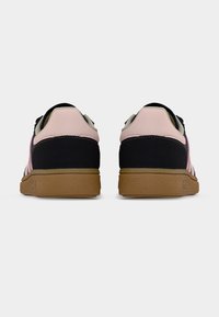 Ζεύγος μαύρων και ροζ χαμηλών αθλητικών παπουτσιών με καφέ σόλες, εμφανιζόμενα από πίσω σε απλό ανοιχτό φόντο.