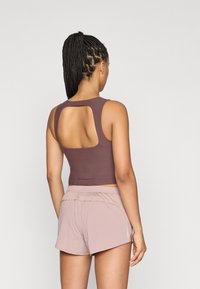 Μωβ κοντό τοπ χωρίς μανίκια με άνοιγμα στην πλάτη, συνδυασμένο με ανοιχτό ροζ σορτς. Το ύφασμα φαίνεται λείο με εφαρμοστή σιλουέτα.